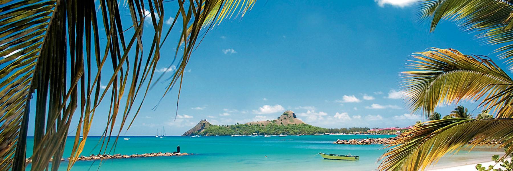 Pigeon Island framed by palm leaves, turquoise sea and boats in St Lucia, a top winter sun destination from the UK.