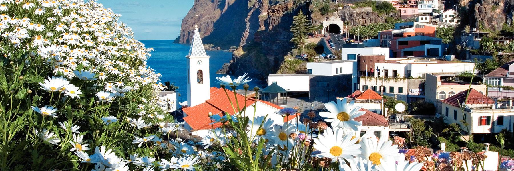 Madeira village with whitewashed church, red-roofed houses and dramatic sea cliffs, ideal for winter sun holidays.