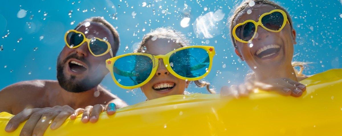 Family of three wearing sunglasses on a last-minute holiday, smiling in the sunshine.