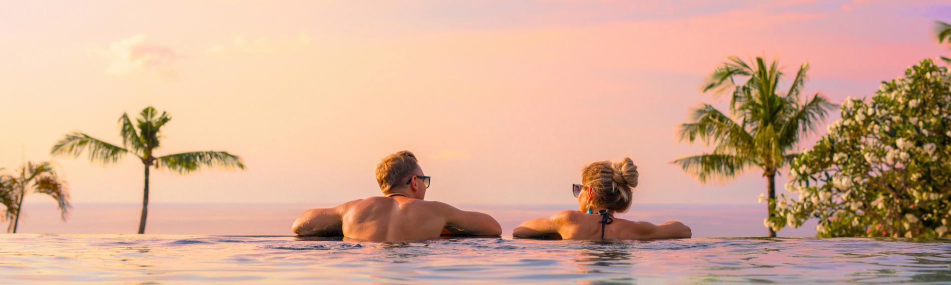 Couple relaxing in an infinity pool at sunset on a luxury long-haul all-inclusive holiday.