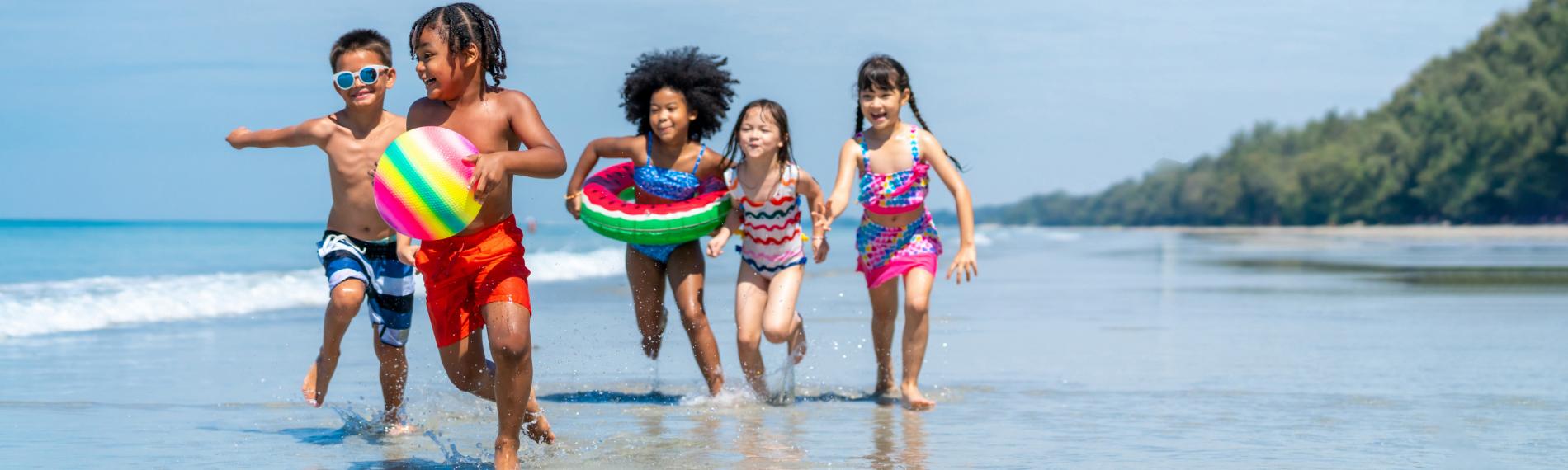 Five happy children on a beach in colourful swimsuits, enjoying a last minute holiday.