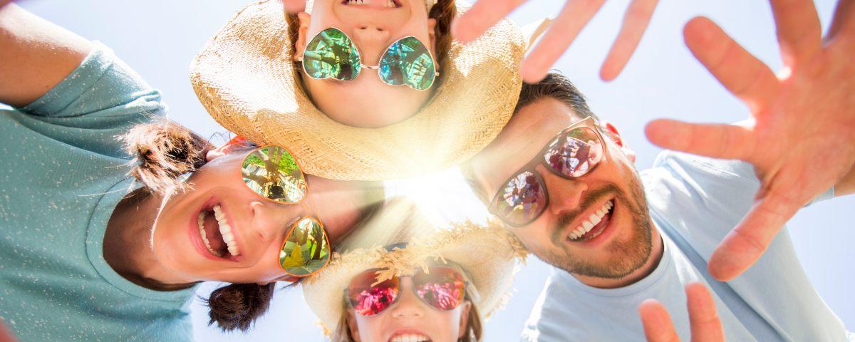 Excited family wearing sunglasses, leaning over the camera and waving