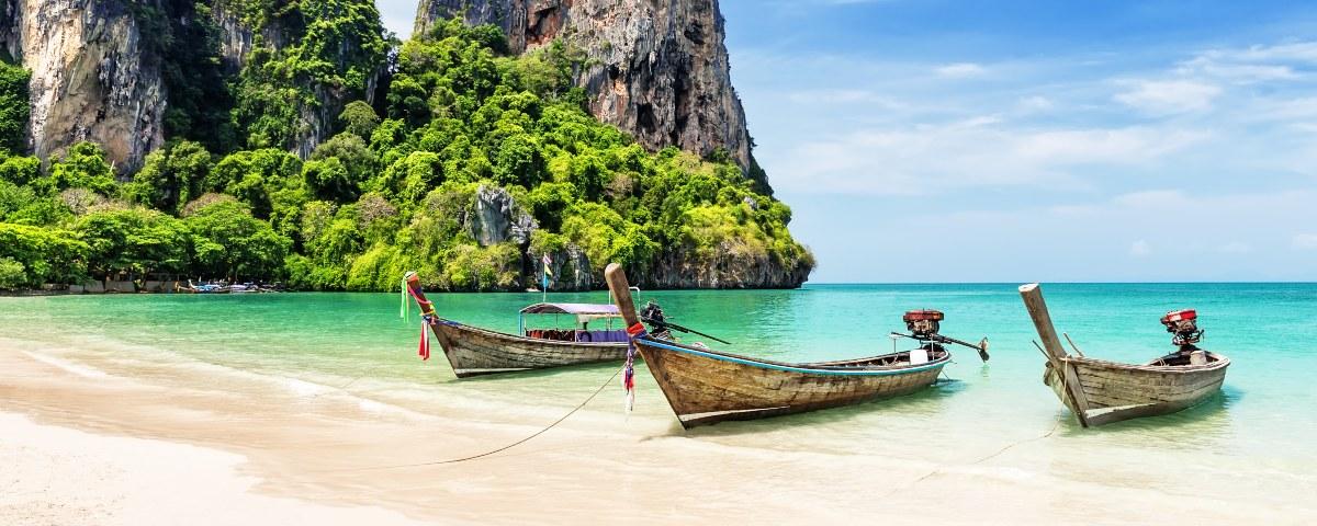A beautiful cliff-backed beach in Thailand with longtail boats sitting in the water