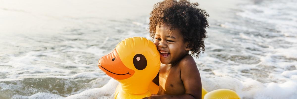Laughing young child sitting in a yellow duck-shaped inflatable at the edge of the sea