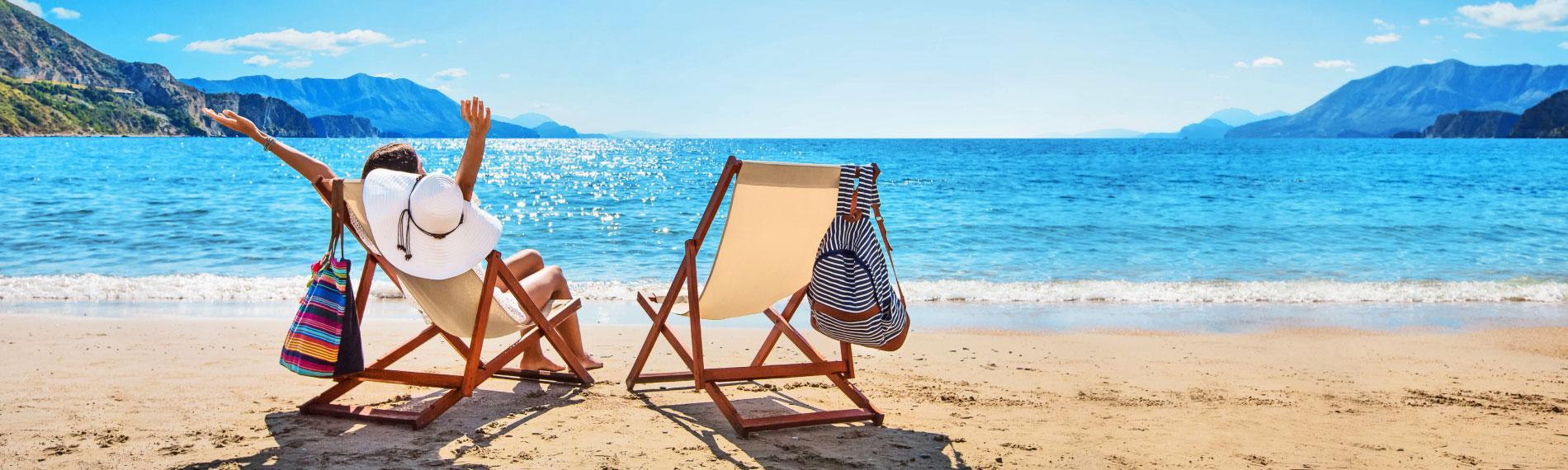 Woman on a sunny sandy beach looking out to sea, reflecting on the challenges of booking a last-minute holiday package.
