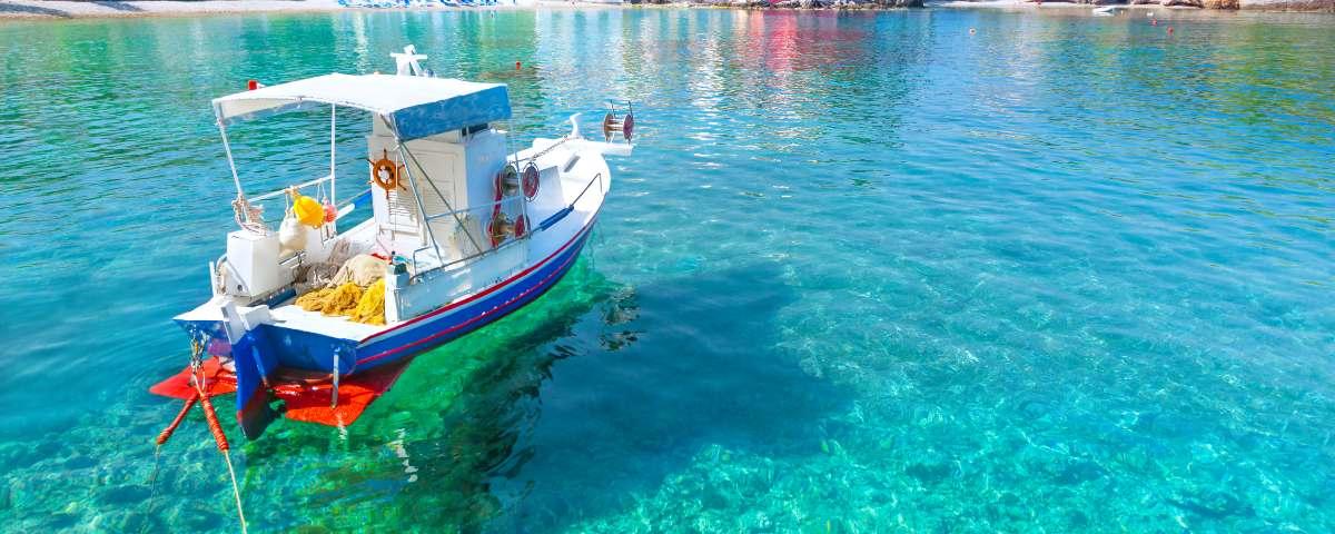 A small blue and white boat bobs on the calm clear waters that lap the coast of Kefalonia in Greece