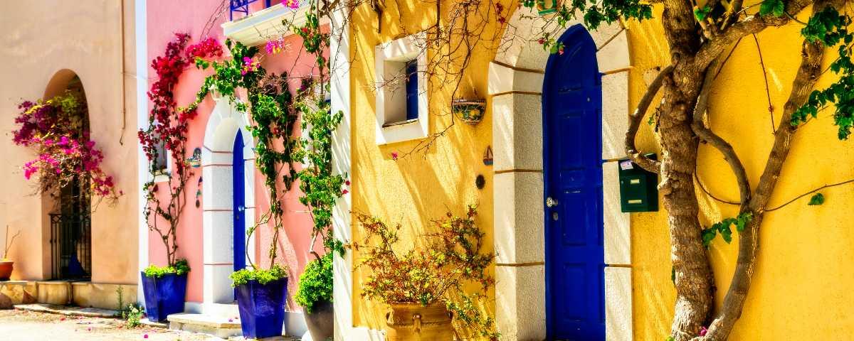 Colourful house fronts in Assos, with arched doorways and climbing plants.
