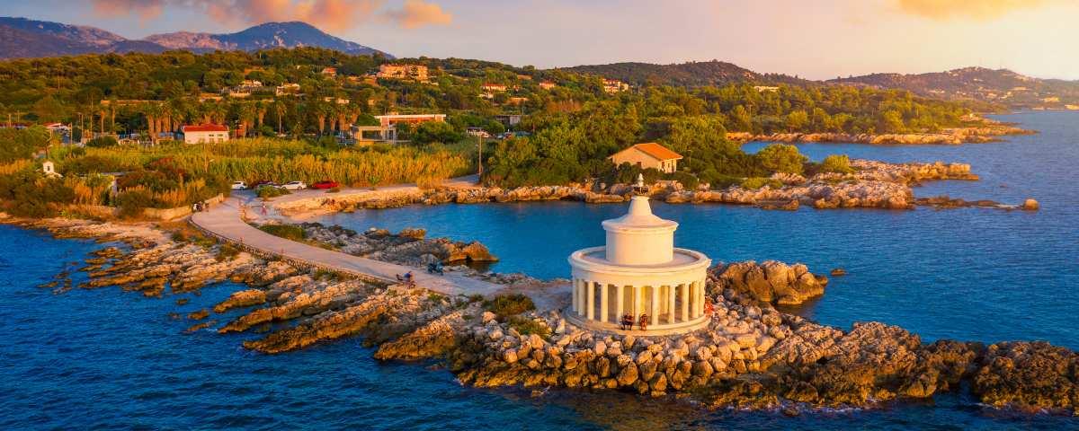 A low white round building with columns creating a sheltered spot to stand and enjoy the view. It doesn't look like the lighthouses we're familiar with in Britain. It's on a small rocky spit that reaches into the sea with a roadway on top, leading back to the wooded coastal area between Argostoli and Lassi.
