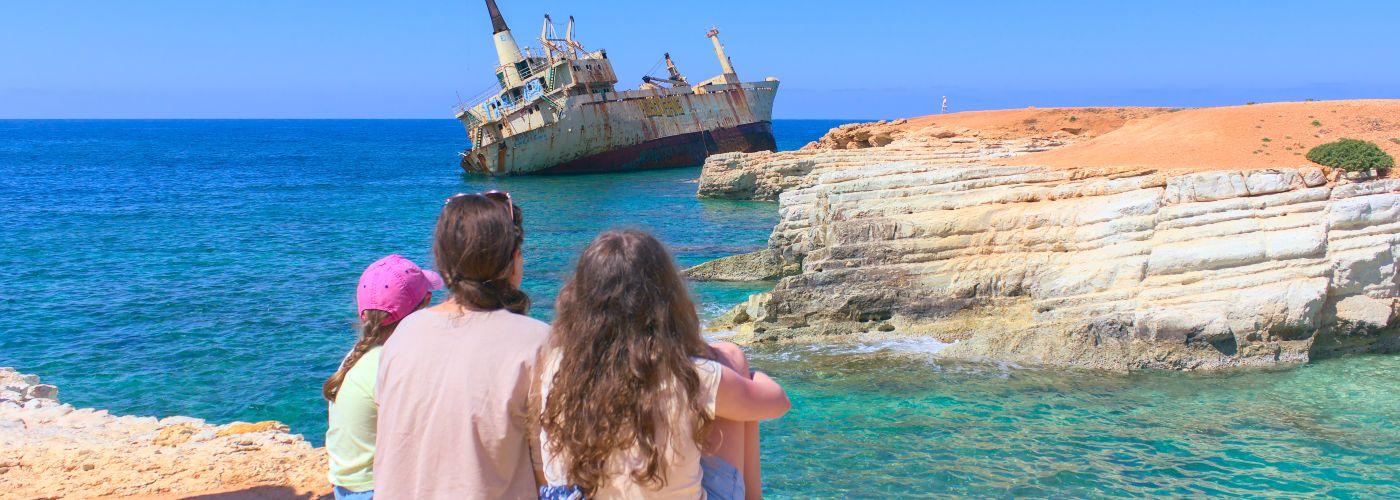 Family admire the view of the rocks and the shipwreck in Paphos, Cyprus