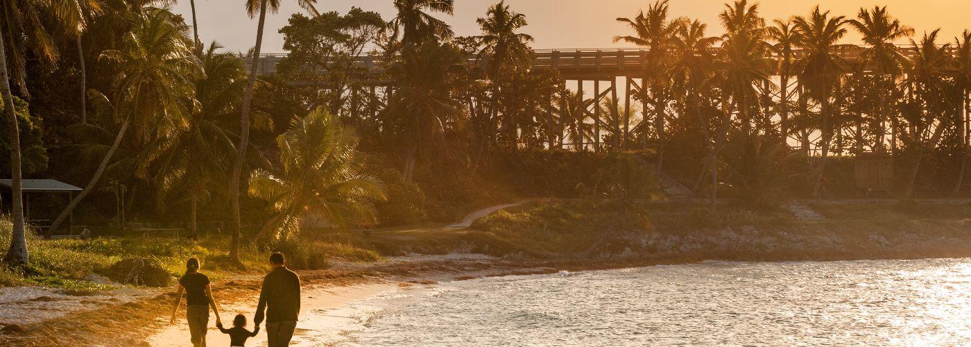 Mum and dad take toddler for a sunset walk on beach in Florida Keys