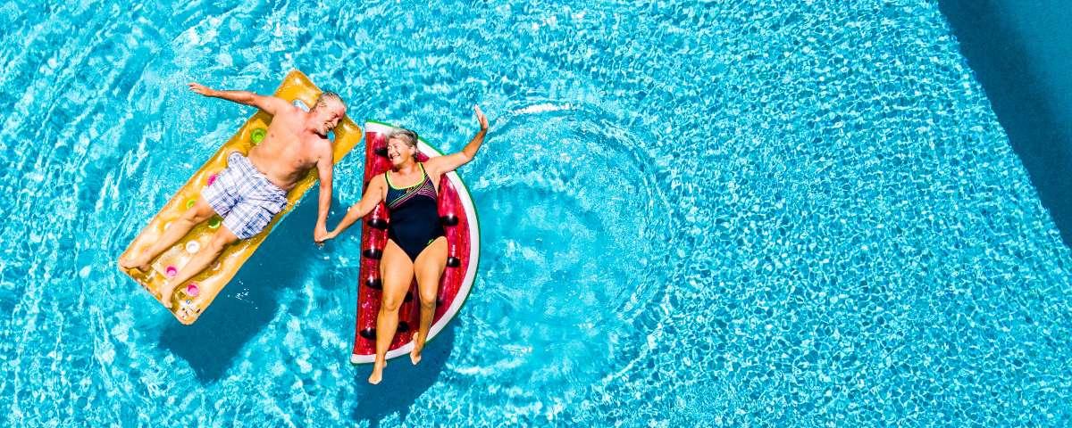 Couple relaxing on novelty lilos in a sparkling swimming pool on holiday