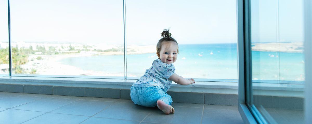 Young toddler, around 1 year old, smiling at the camera on a balcony with a view of the Mediterranean, beach and blue sky