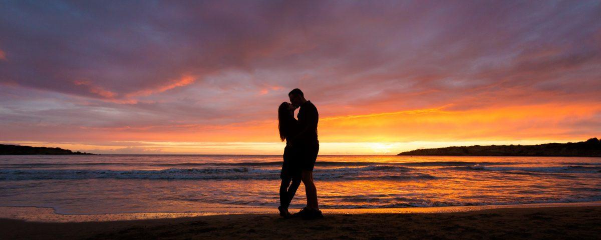 A couple on the beach at Coral Bay, Cyprus, sharing a kiss in silhouette against the sunset