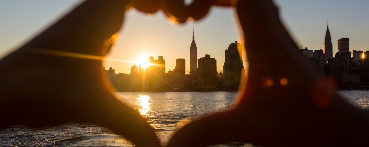 A couple's hands frame the sunset over the New York skyline by making a heart shape together