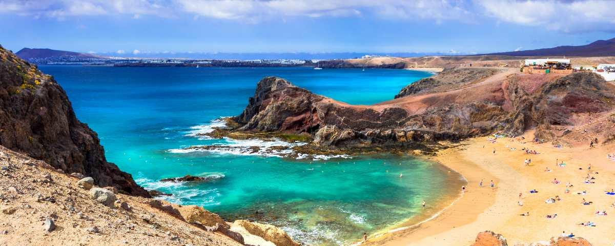 Golden sands and turquoise waters of Papagayo beach, with the blue sea and a view along Lanzarote's coast in the background.