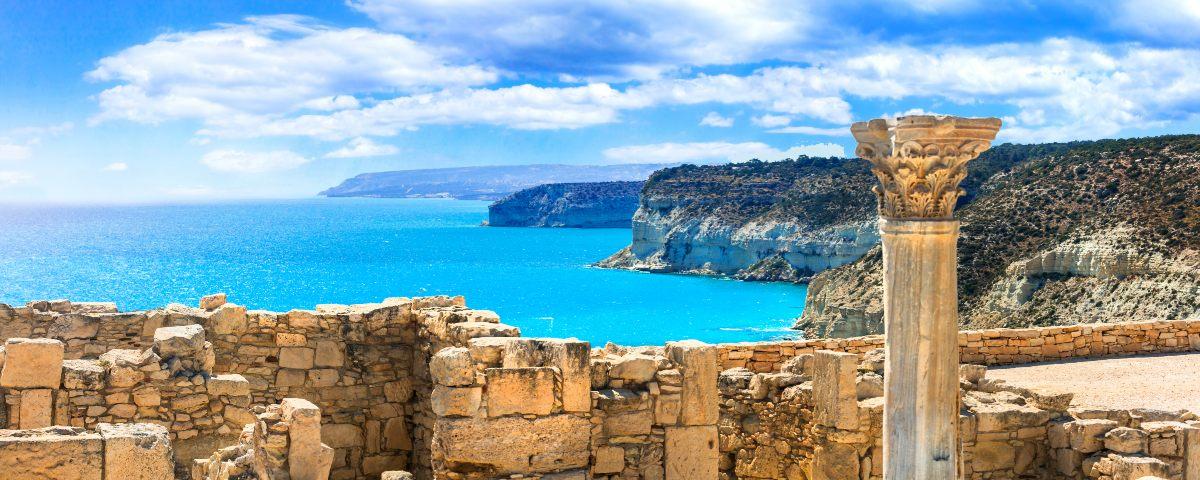 Ancient temple ruins at Kourion against a backdrop of the blue sea and sky with fluffy white clouds and a dramatic cliff coastline