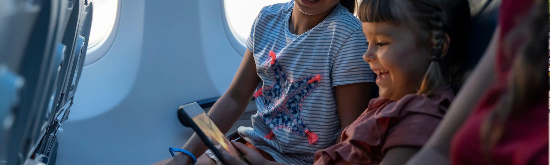 Two girls sat on a plane watching a tablet