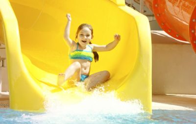 Happy young child about to splash down from a big yellow waterslide at sunny Aqualava waterpark in Playa Blanca, Lanzarote, Spain