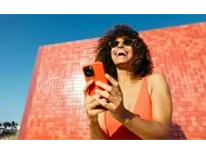 Smiling woman in sunglasses using her phone against a red tiled wall and blue sky.