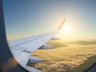 Airplane wing flying above the clouds, illustrating an article about the holiday travel impact of global jet fuel shortages.