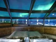 Northern Lights glowing above a glass-roofed cabin bedroom in Lapland, Finland.