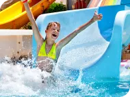 Child with arms raised sliding into a pool from a blue waterslide at a waterpark.