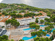 Whitewashed Mediterranean resort with outdoor pools, sun loungers and pine woodland, ideal for an August holiday.