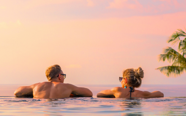 Couple relaxing in an infinity pool at sunset on a luxury long-haul all-inclusive holiday.